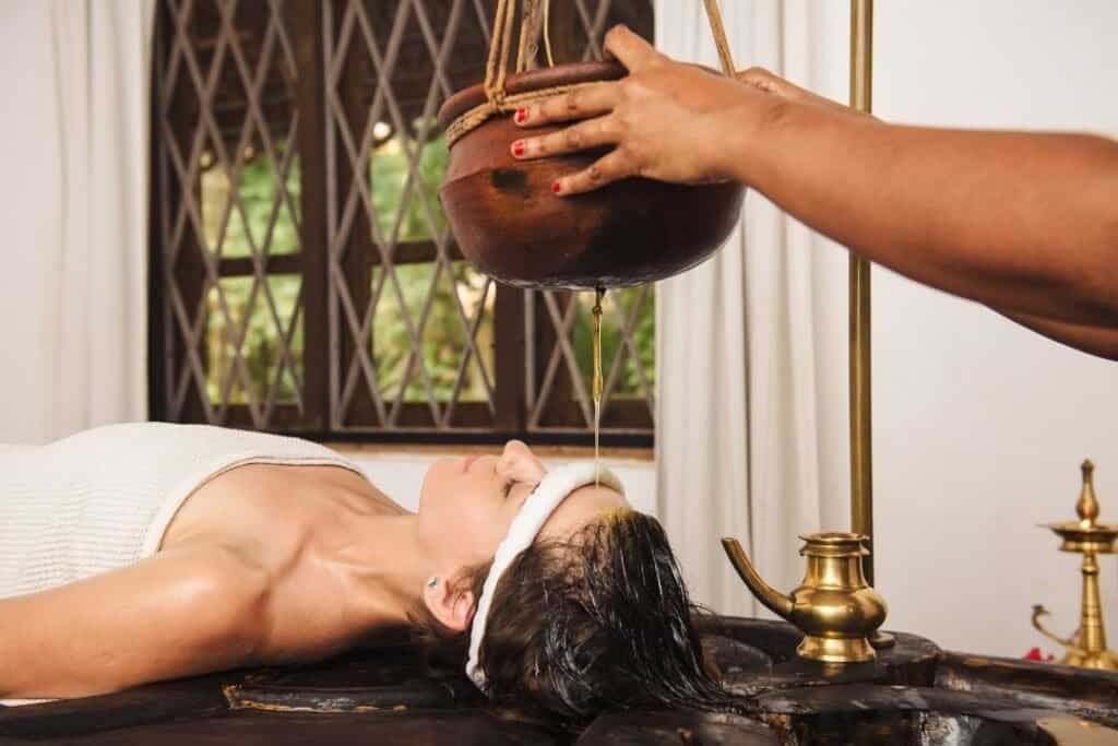 Kalari massage therapy session with herbal oil pouring on the forehead in a traditional Ayurvedic setting.
