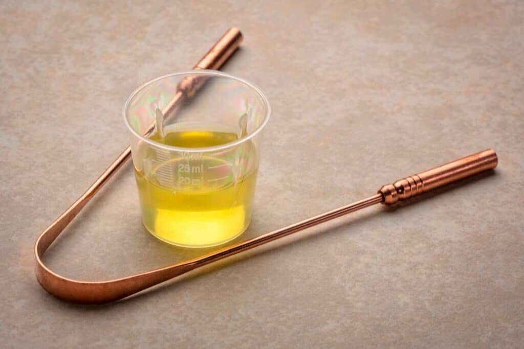 Energizing Ayurvedic herbal oil in a measuring cup with copper tools on a textured surface.