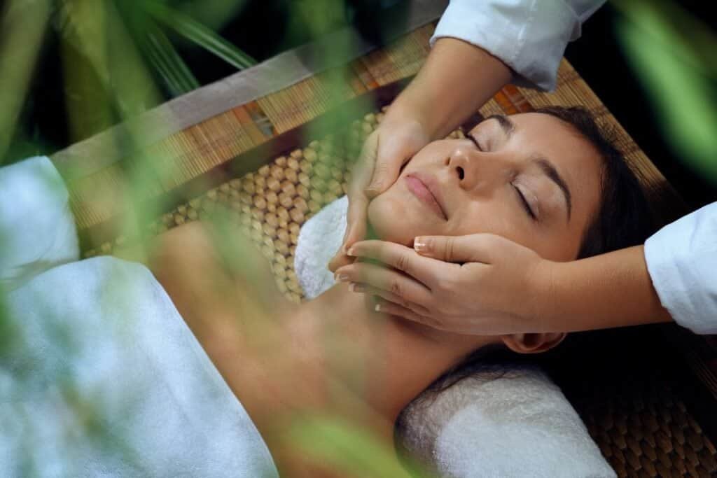 Relaxing woman receiving facial massage during Ayurveda or yoga wellness session.