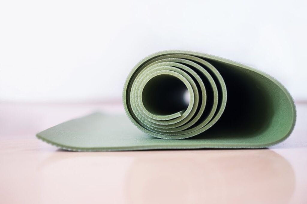 Soft green yoga mat rolled up on a light wooden surface, promoting relaxation and mindful practice.