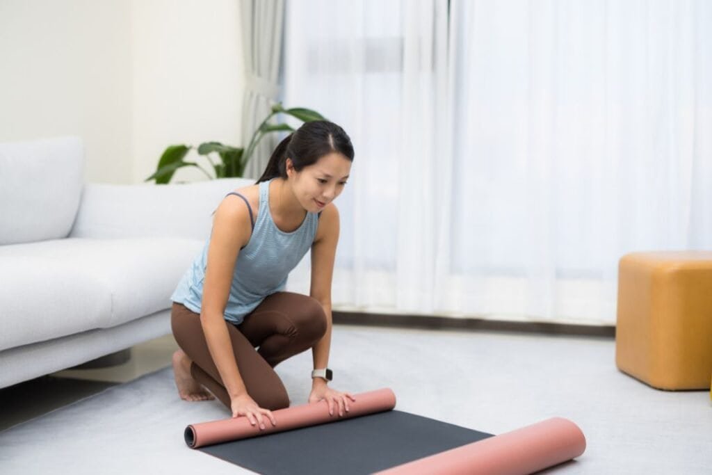 Yoga practitioner preparing her mat in a cozy, bright living room with natural light and indoor plants.