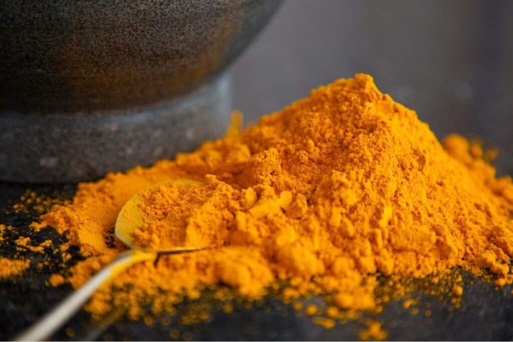 Finely ground turmeric powder on black surface with a silver spoon near the pile. for turmeric spice recipe.