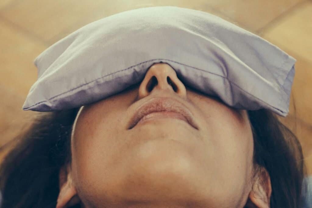 A woman resting with a pillow on her forehead, practicing relaxation techniques at Ayurveda Yoga Life wellness center.